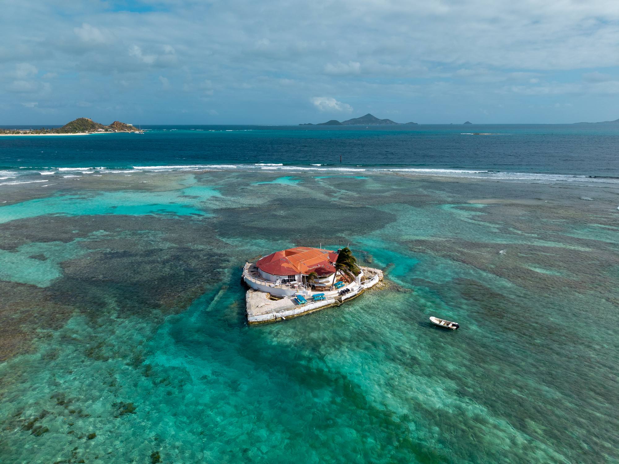 Aerial view of a reef with a lone red-roofed islet in the Grenadines