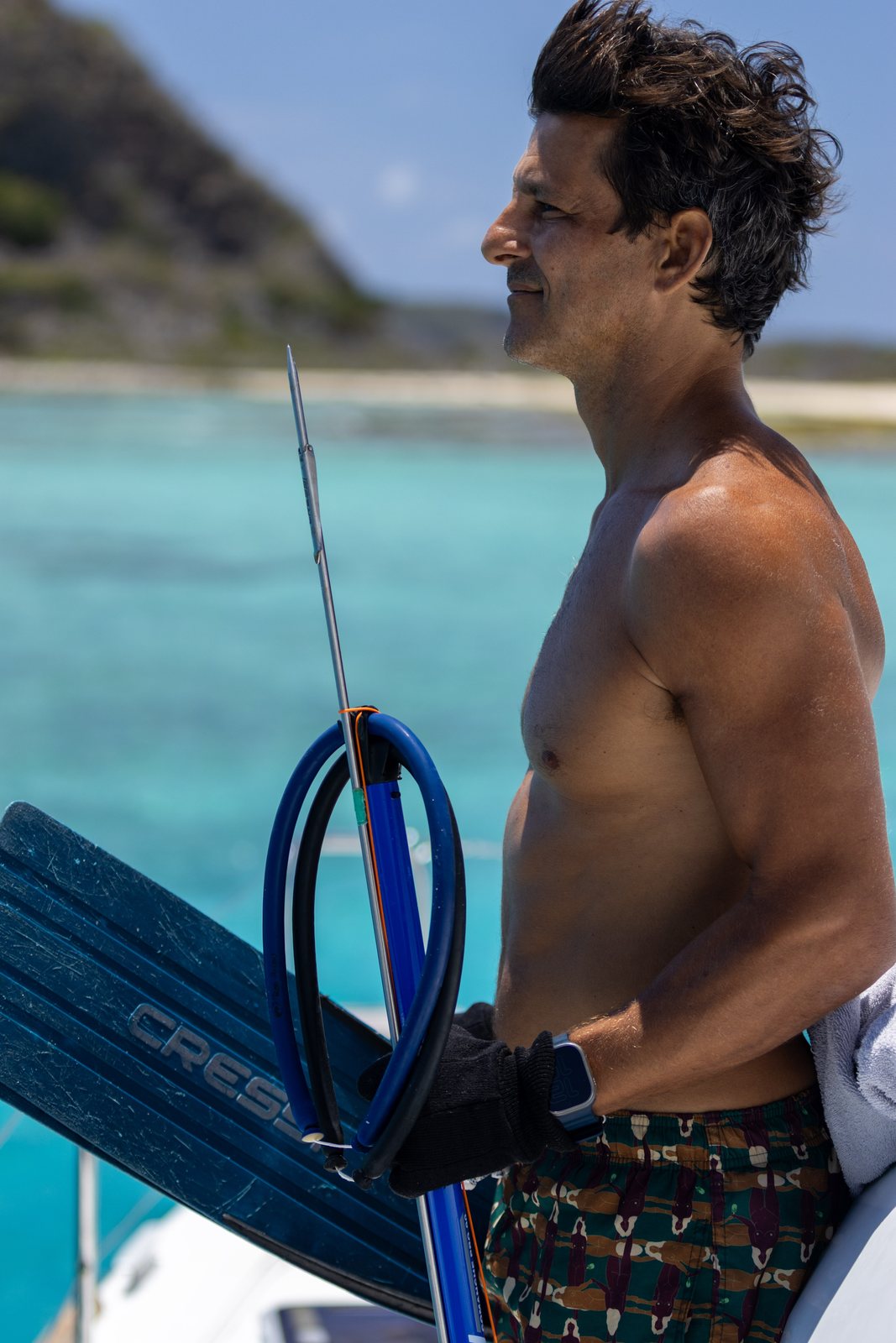 Guest holding a speargun and fins by a turquoise lagoon