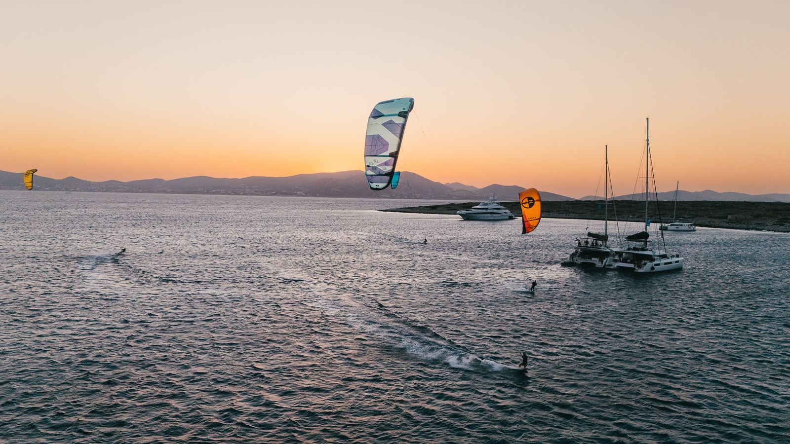 Aerial view of kitesurfers around anchored catamarans at sunset
