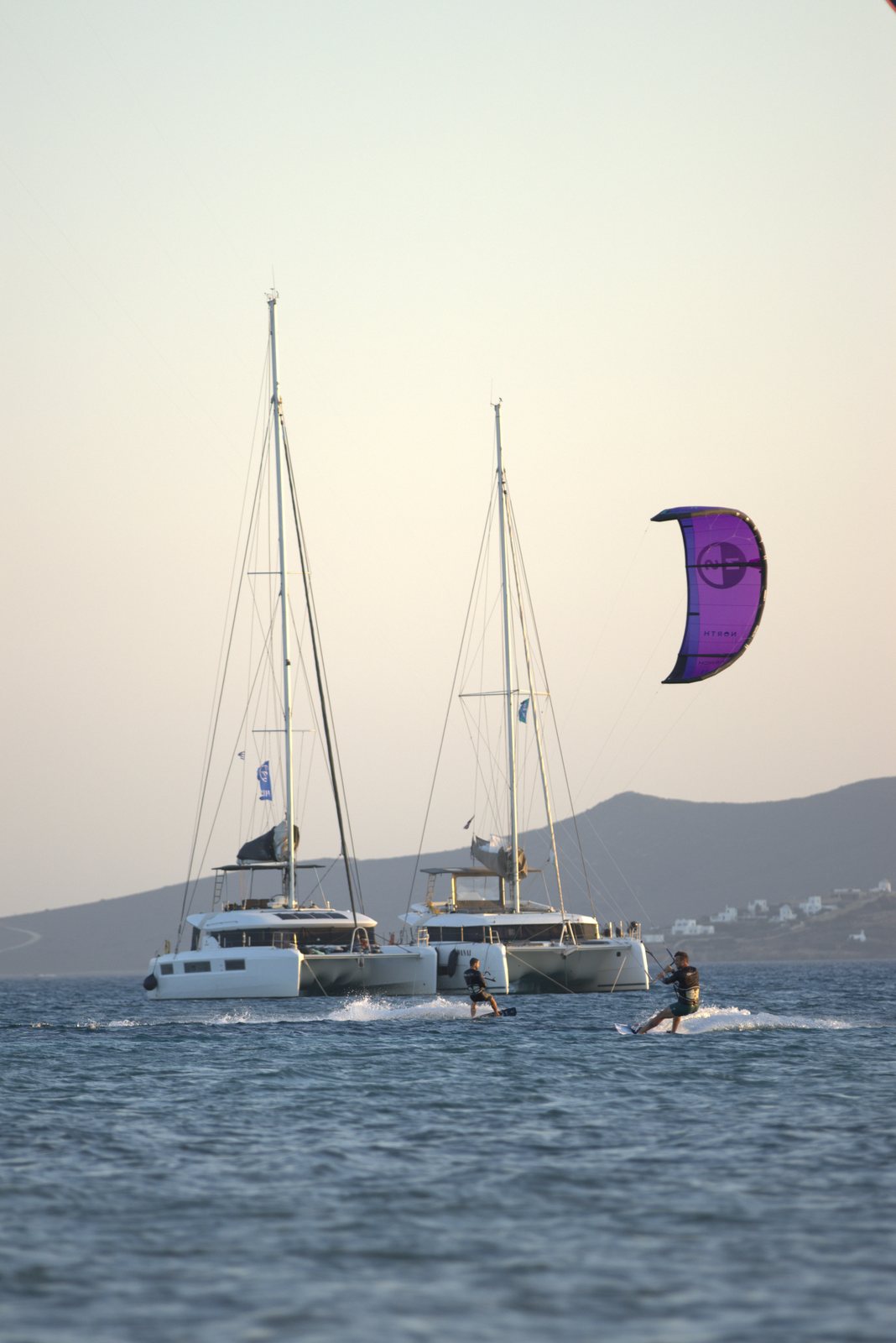 Kitesurfer riding past two anchored catamarans