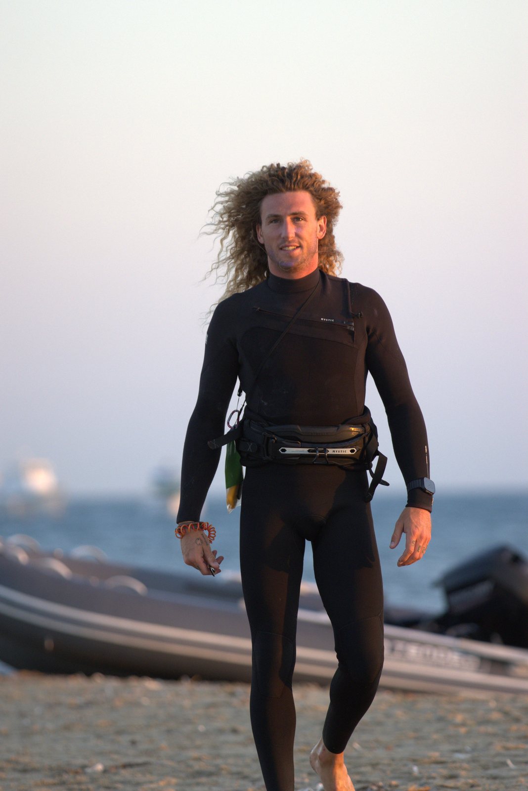Guest walking up the beach in a wetsuit after a session