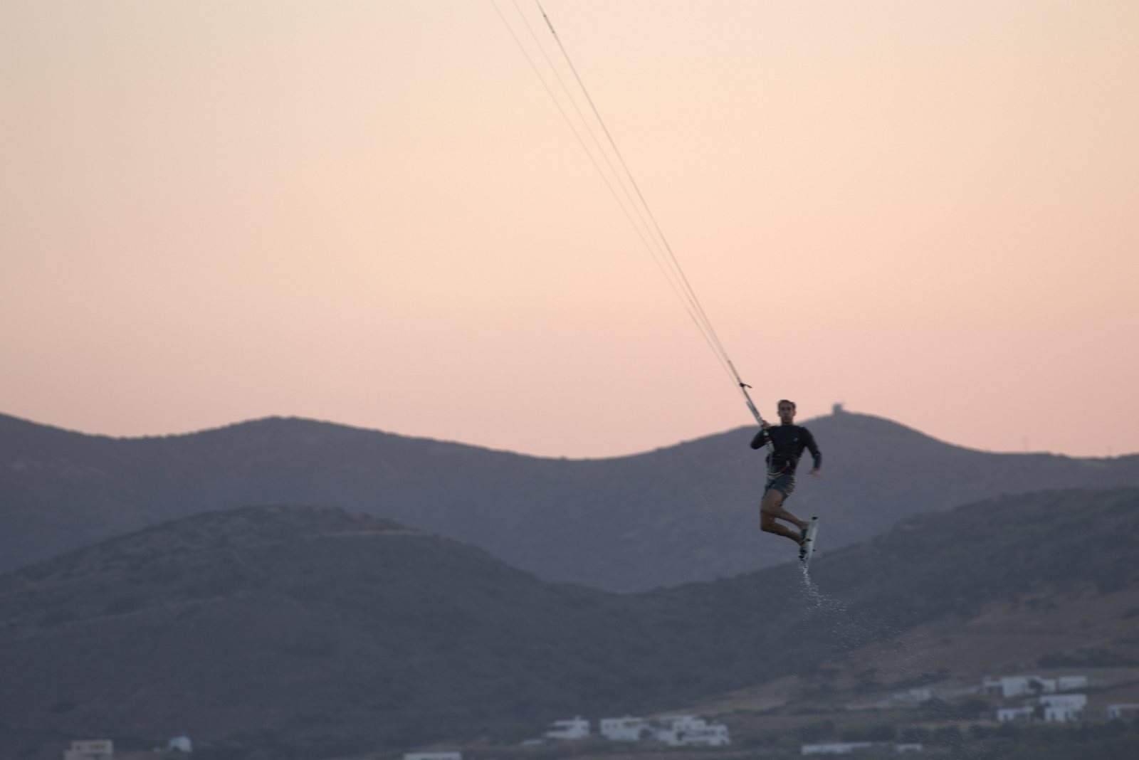 Kitesurfer jumping high above a hillside bay